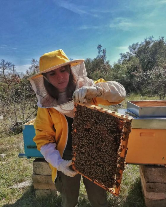 Ragazza in tuta da apicoltore regge un'arnia tra le mani